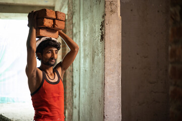 A DAILY WAGE LABOURER CARRYING BRICKS ON HEAD FOR CONSTRUCTION