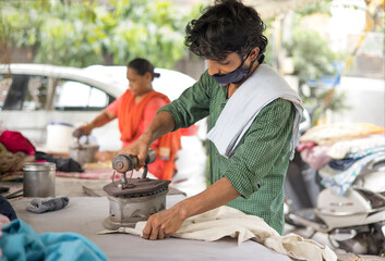 A LABOURER IRONING CLOTHES WEARING FACE MASK
