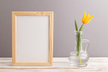 Wooden frame with orange tulip flower in glass on gray pastel background. side view, copy space, mockup.