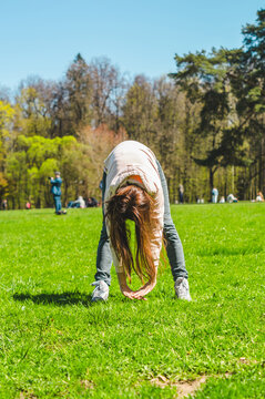 woman doing exercises outdoors on the grass in city park. exercising to bending over to the ground