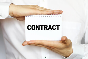 A businessman in a white shirt shows a business card with text CONTRACT , copy space, business concept