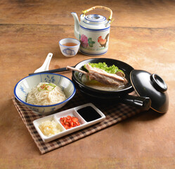 double boiled herbal bak kut teh pork ribs soup in black clay hot pot with rice and vermicelli noodle on wood table and sauces halal asian menu