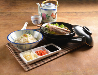 double boiled herbal bak kut teh pork ribs soup in black clay hot pot with rice and vermicelli noodle on wood table and sauces halal asian menu