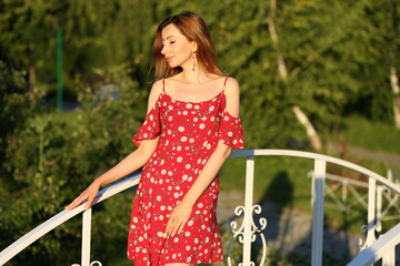 Beautiful woman in red dress standing on white bridge in the park