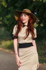 A happy woman, holding a wide hat, poses in a park in summer