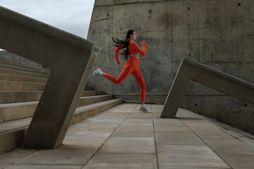 Young female athlete with neon orange sportswear running down a flight of stairs. Caucasian woman jogging in modern city.