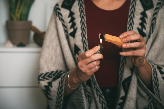 woman lighting a palo santo dressed with a handmade poncho. background with copy space. meditation concept