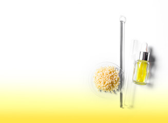 Candelilla Wax in Chemical Watch Glass, yellow cosmetic liquid (oil) and test tube place next to stirring rod. Chemicals for beauty care on yellow background. (Top View)