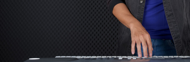 Closeup musician's hand playing on a music keyboard player in front of black soundproofing walls. Musician producing music in professional recording studio.