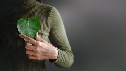 Green Energy, Renewable and Sustainable Resources. Environmental and Ecology Care Concept. Close up of Hand Holding a Heart Shape Green Leaf on Chest - obrazy, fototapety, plakaty