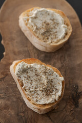 Ciabatta slices with cream cheese and herbs on olive wood board