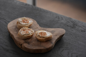 Baguette slices with cream cheese and herbs on olive wood board