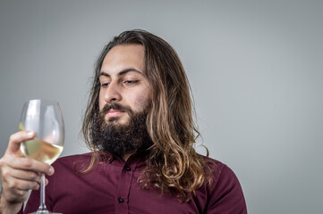 portrait of a young middle eastern businessman with beard and long hair holding a glass of fresh white wine