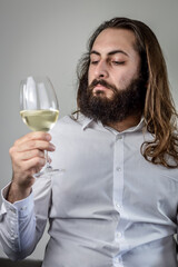 portrait of a young middle eastern businessman with beard and long hair holding a glass of fresh white wine and looking at its color