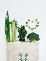 Top view of green vegetables in an eco cotton tote bag on a white background.