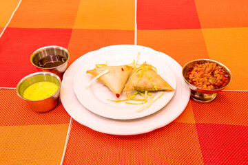 two vegetable samosas served in a Pakistani restaurant with sauces on an orange tablecloth