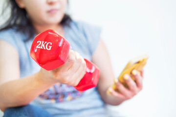 Fat woman exercising by lifting red dumbbells and watch teaching from trainers through smartphones