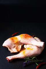 Food concept raw chicken quarters with spices on black slate stone board with copy space