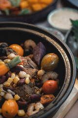 Roasted beef in pot with vegetables, cherry tomatoes, chick peas and shrimps served with other dishes in restaurant ready to eat. Healthy dinner in Moroccan or Portuguese style restaurant decorated