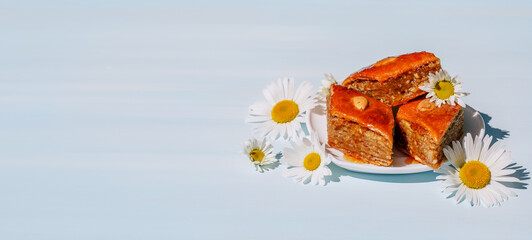 Diamond shaped baklava made of puff pastry and honey on a blue table on a sunny summer day. Traditional oriental sweets with nuts. Horizontal photo, banner.
