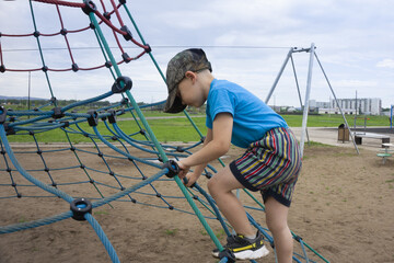 A little boy in a blue T-shirt and colorful striped shorts is fearlessly climbing up the rope...