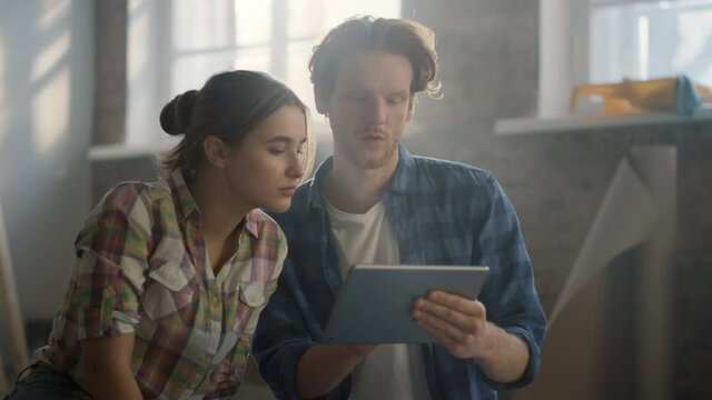 Happy couple discussing design ideas indoors. Woman pointing to tablet screen.