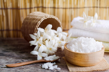 Closed up white spa salt in wooden bowl and spoon over blur soft white towel and fragrance flower...