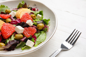Plate with tasty grapefruit salad on light wooden background, closeup