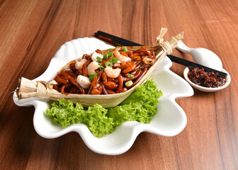 stir fried hokkien dark soy sauce udon noodle with seafood and meat in leaf on wood table asian...