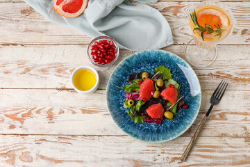 Plate with tasty grapefruit salad and glass of lemonade on light wooden table