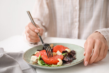Woman eating tasty grapefruit salad at light table, closeup