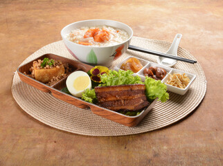 double boiled pumpkin rice congee porridge with braised pork belly , egg, fried bean curd tofu and peanut sour vegetable bento set on wood table asian halal menu