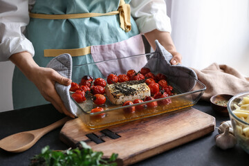 Woman holding dish with baked tomatoes and feta cheese in kitchen