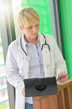 Portrait Of A Female Doctor  Reading A Medical Report On His Tablet  While She Is Giving Instructions On His Mobile Phone