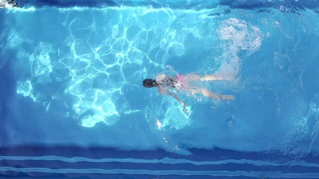 AERIAL: a girl in a bright swimsuit learns to swim alone and holds her nose with her hand for diving in a pool with crystal blue water. spin and fool around in an empty pool. 
summer holidays resort