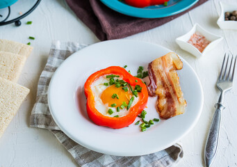 Breakfast, fried egg in red sweet pepper with bacon on a white ceramic plate on a light concrete background.
