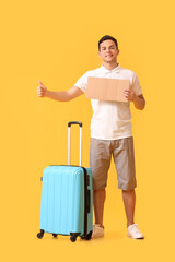 Young man with cardboard and suitcase hitchhiking on color background