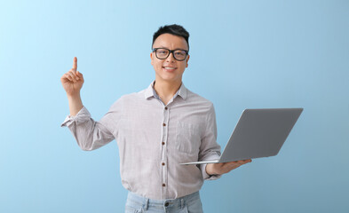 Portrait of Asian teacher with laptop and raised index finger on color background