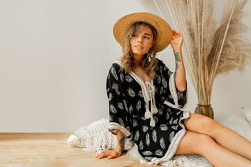 Pretty blond woman in straw hat and boho dress  posing in studio over white background  with pampas...