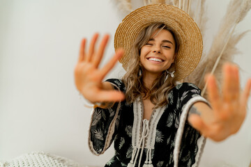 Playful cheerful woman in straw hat pull hands to the camera.  White background.  Boho outfit....