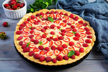 Delicious homemade tart with strawberries and raspberries garnished mint leaves on wooden background