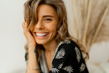 Close up portrait of  blond woman with perfect smile in stylish boho autfit. Posing in inerior...