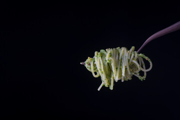 Spaghetti with green pesto sauce made with wild garlic rolled on a fork. Isolated over black background