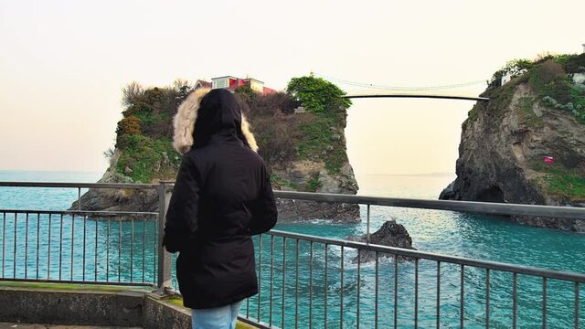 Girl watching a bridge that links the island house to the mainland in Newquay. A young woman travelling by The Island House Bridge near Great Western Beach in Newquay, Cornwall, England in 4K. 