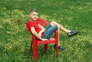 Boy sitting on a red chair in the field