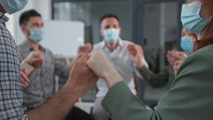 male and female work team wearing medical masks raise and lower their arms while sitting in a circle during a motivational session - Powered by Adobe