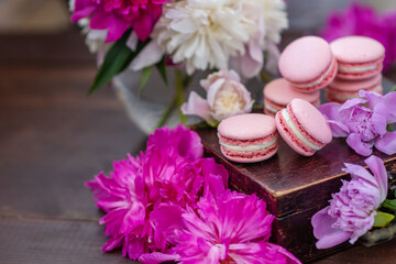 Obraz na płótnie Canvas Pink macaroons lie on a wooden box surrounded by peony flowers