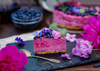 piece of berry dessert lying next to a mug of tea, violet flowers and a background of peonies