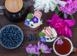 Obraz na płótnie Canvas Berry dessert in cups with violet flowers, macarons, and on a background of peonies