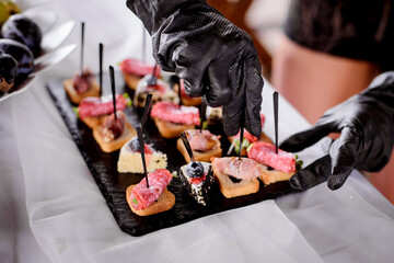 Hands in black gloves serves sandwiches. Catering